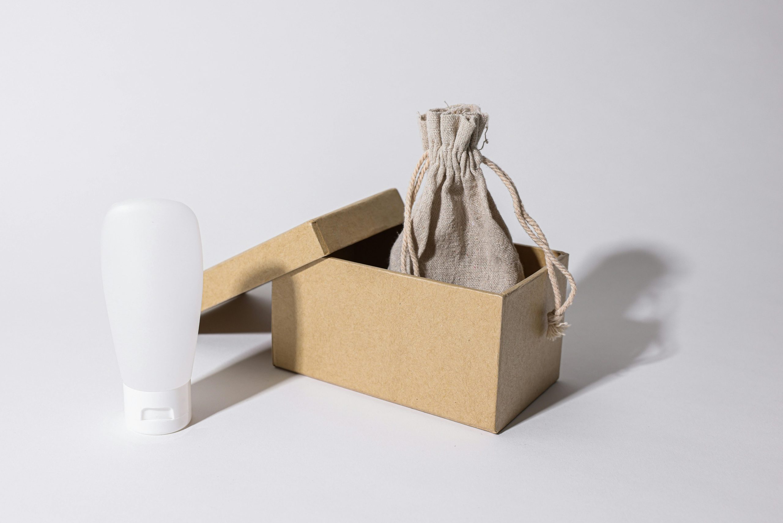 Minimalist photo of eco-friendly packaging with a cardboard box, pouch, and white plastic bottle.